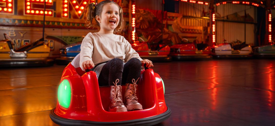 A photo of a young girl riding a red bumper car with fairground dodgems behind her