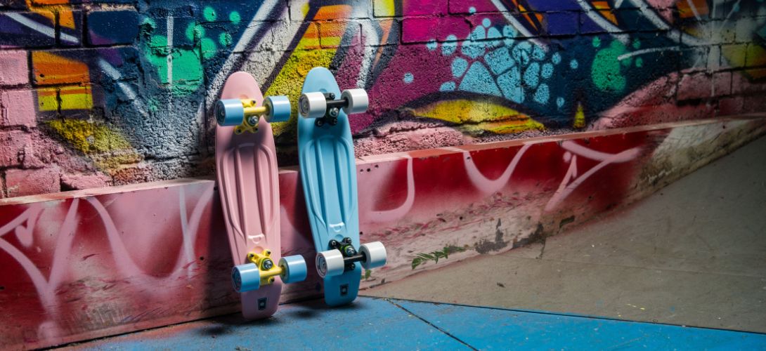 A photo of two pastel pink and pastel blue cruiser skateboards rested against a graffiti wall