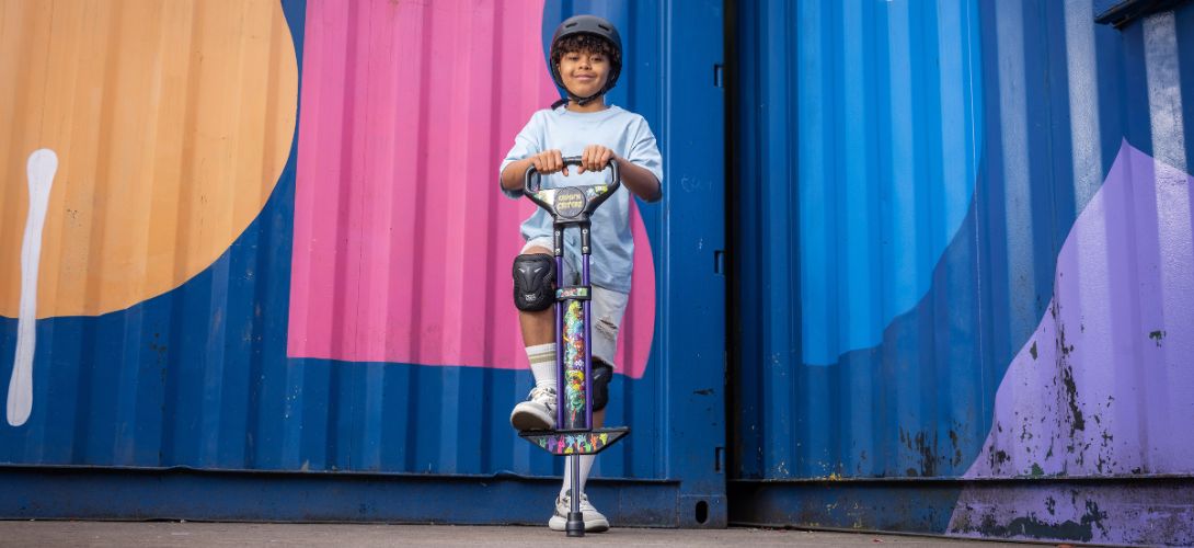 A photo of a boy with his foot on a pogo stick against a corrugated metal graffiti background