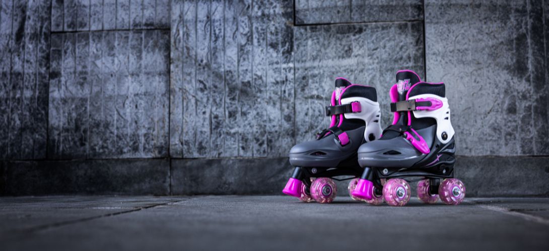 A pair of black and pink quad skates against a grey brick background